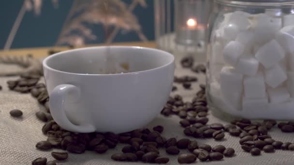 Café se vierte en una taza blanca, granos de café, un recipiente con azúcar refinada — Vídeo de stock
