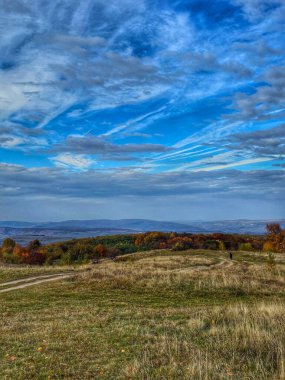 Mavi gökyüzü ve beyaz bulutlarla dolu güzel bir günde tepelerin, ormanların ve dağların güzel sonbahar manzarası. Salicea, Cluj, Romanya