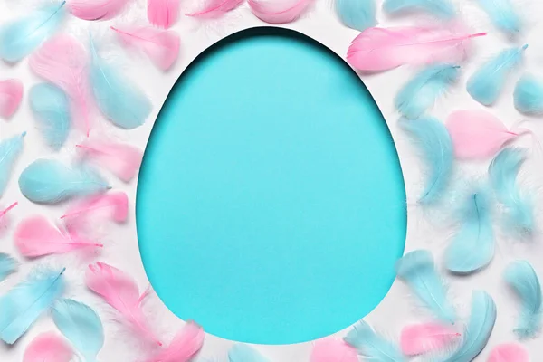 Blue easter Egg shaped hole with copy space. Creative layout with colored feathers pattern. Happy easter concept, greeting card