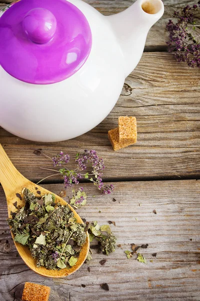Dry herb tea in a wooden spoon and white teapot