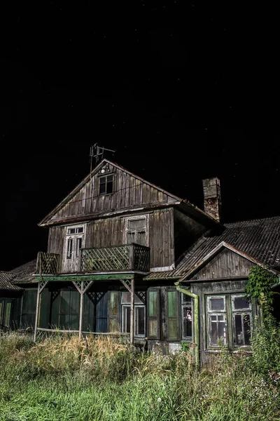 Eski ürkünç terk edilmiş ahşap ev kara gece arka planında aydınlatılmış.