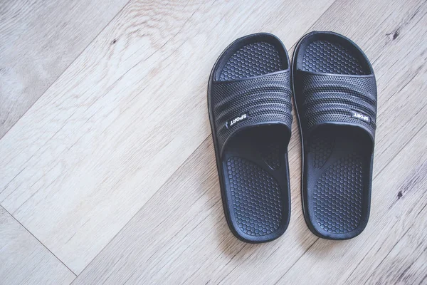 Pair of black men flip flops on wooden floor with copy space