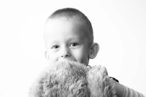 3岁的男孩摆姿势 泰迪熊抱着一只泰迪熊 看着摄像机 微笑着面对着白墙 黑白照片 — 图库照片