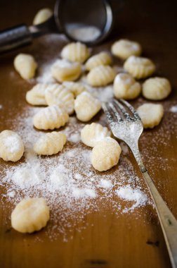 Taze pişmemiş gnocchi un ahşap bir tahtanın üzerinde çatal ve arka planda süzgeç ile birlikte..