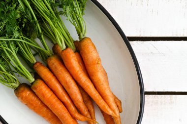 Beyaz ahşap arka planda beyaz tepside yapraklı turuncu havuçlar. Üst manzara..