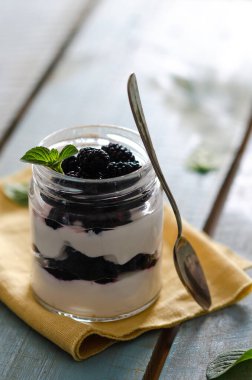 Böğürtlenli yoğurt ve kavanozdaki nane yaprakları sarı peçete ve açık mavi ahşap zemin üzerinde.. 