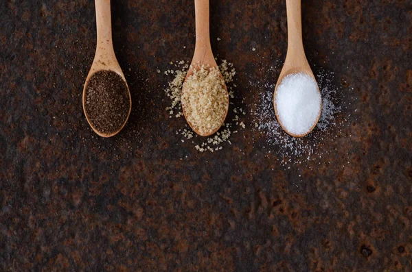 Kahverengi, muscovado ve siyah bir zeminde tahta kaşıklarda normal şeker.. 