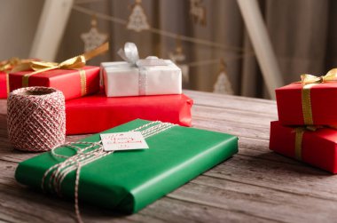 Noel hediyeleri, yeşil, kırmızı ve beyaz kağıtlarla sarılmış tahta bir masa ve arkasında beyaz bir Noel ağacı..