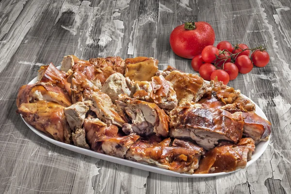 Bord van Spit geroosterd varkensvlees segmenten met bos van tomaat op oude houten achtergrond — Stockfoto