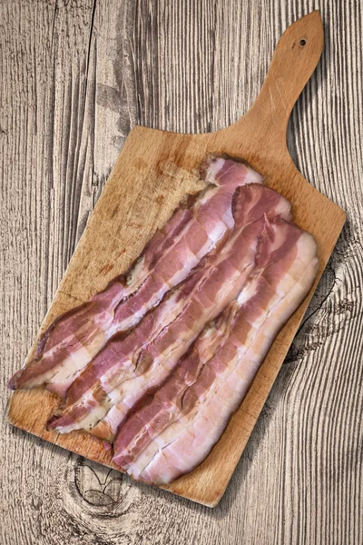 Tabla de cortar con arandelas de vientre de cerdo en fondo de madera vieja —  Fotos de Stock