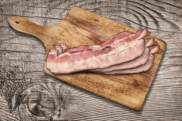 Tabla de cortar con arandelas de tocino de vientre de cerdo en fondo de madera — Foto de Stock