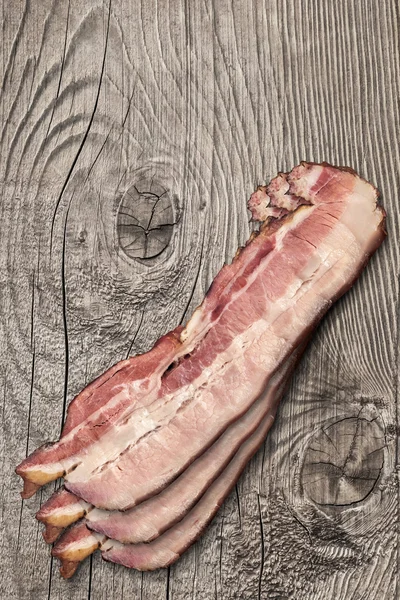 Rasher di pancetta di maiale sulla superficie del tavolo in legno annodato vecchio — Foto Stock