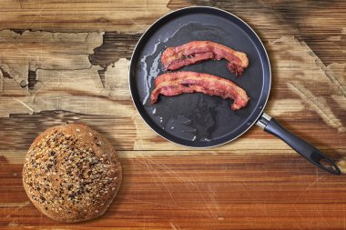 Fried Bacon Rashers in Teflon Frying Pan with Integral Bread Loaf on old Wooden Table