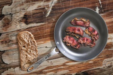 Fried Pork Ham rashers in Teflon Frying Pan with slice of Bread on old Wooden Table