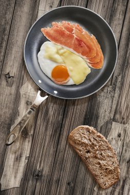 Prosciutto Rashers sahanda yumurta ve Edam peynir Teflon tavada ekmek dilimi eski ahşap masa kırık