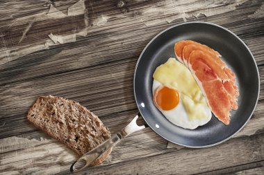 Prosciutto Rashers sahanda yumurta ve peynir ekmek dilimi eski tavada ahşap masa kırık