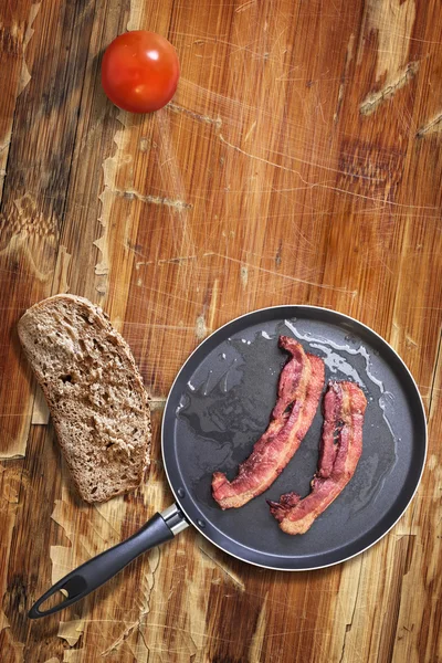 Fried Bacon Rashers in Frying Pan with Tomato and Bread slice on Old Wooden Table — Stok fotoğraf