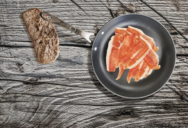 Prosciutto plakken in Teflon koekenpan met sneetje brood op zeer oude gebarsten houten tafel — Stockfoto