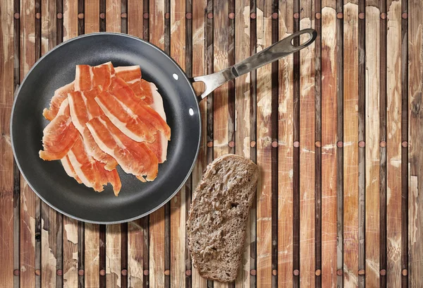 Gerookte ham Ham segmenten in Teflon koekenpan met segment van brood op oude verweerde gepeld uit houten placemat — Stockfoto