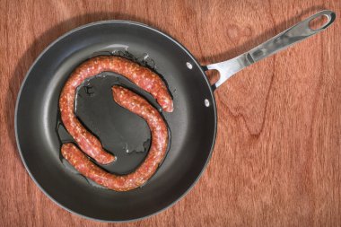 Teflon tavada ahşap arka plan üzerinde ham ev yapımı sosis