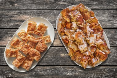 Platefuls peynir pasta Gibanica ve Spit kavrulmuş domuz eti dilim eski ahşap Bahçe masa yüzeyi