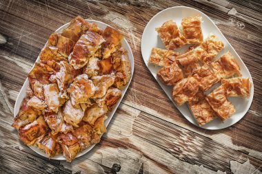 Platefuls peynir pasta Gibanica ve Spit kavrulmuş domuz eti dilim eski ahşap Bahçe masa yüzeyi