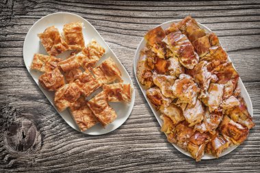 Platefuls peynir pasta Gibanica ve Spit kavrulmuş domuz eti dilim eski ahşap Bahçe masa yüzeyi