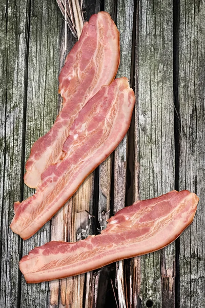 Rashers de bacon de porco no fundo de madeira rachada de nós velhos — Fotografia de Stock