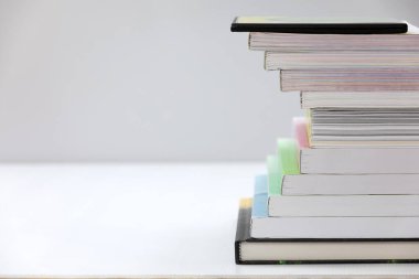 Gri arkaplanı olan beyaz bir masanın üzerinde bir yığın kitap var. Sol tarafta boş bir alan var.