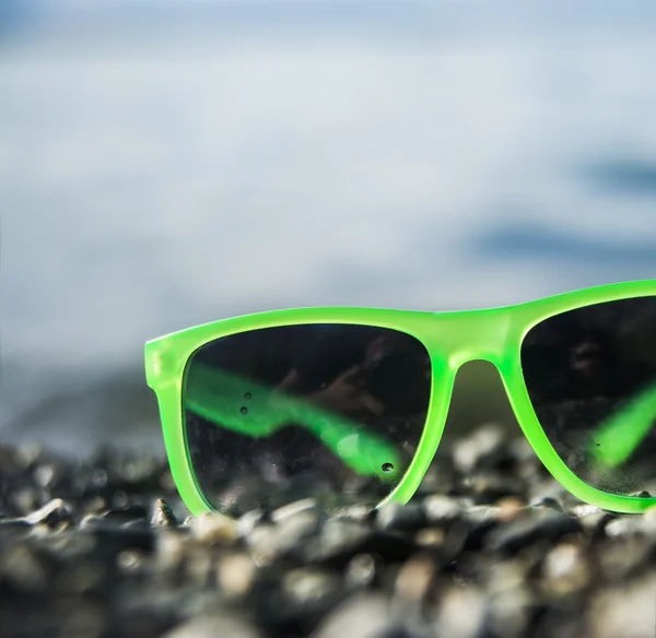 Green sunglasses on pebble ground — Stock Photo, Image