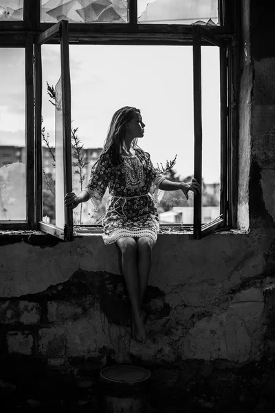 汚れたガラス近くの窓辺に座っている若い大人の女性の完全な長さの肖像画 — ストック写真