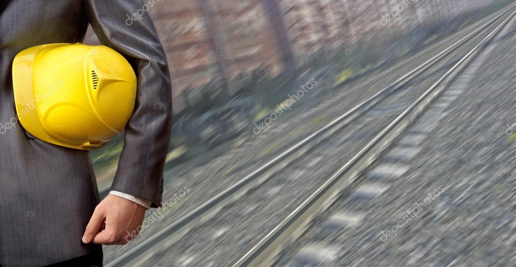 Torso engineer or worker hand holding yellow helmet for workers security against the background of an railway with arc legs and rails for trolleys with coal in perspective Logistic idea concept