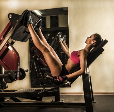 Çekici genç kadın vücut geliştirme bir spor salonunda yapıyor. Bacak kasları pompalama.