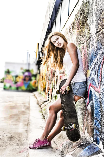 portrait of teen girl with long skate board stand against  wall.