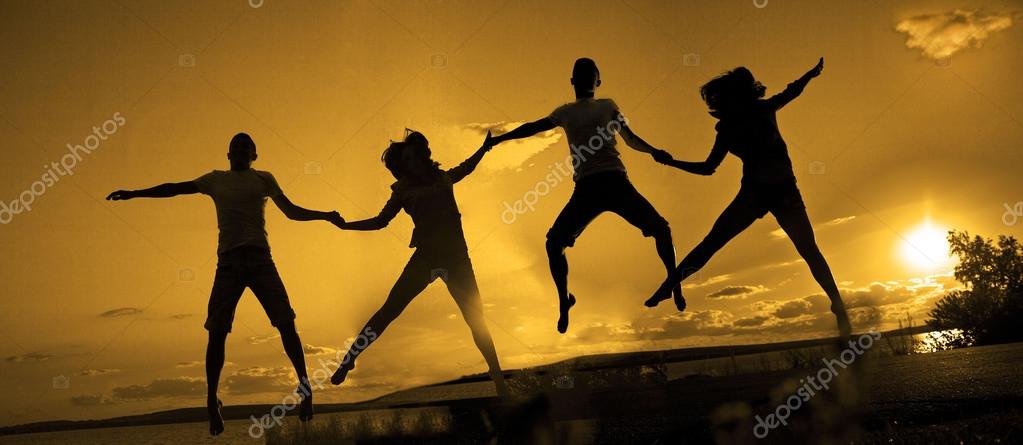 Group of four happy young people holding hands, dancing and jumping in air