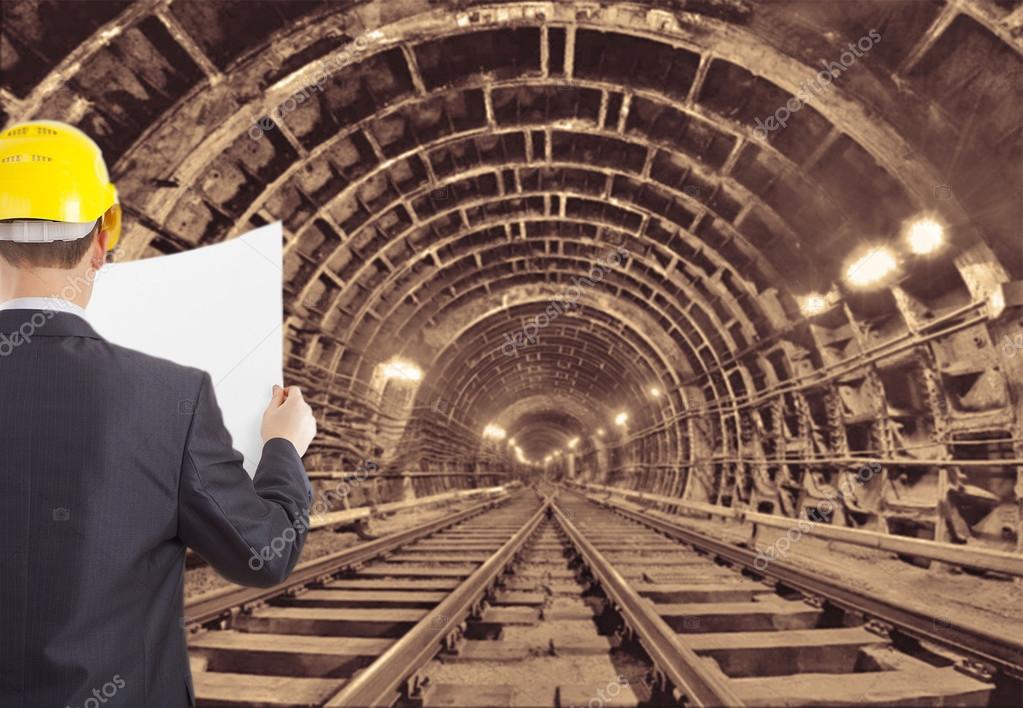 Engineer hand wear yellow helmet for workers security holding empty blue print paper document against  background of an underground mine with arc legs and rails for trolleys with coal in perspective