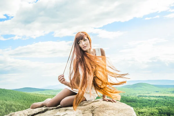 石の上に座ってセクシーな女性 崖の端に座っている髪の長い若い女性 — ストック写真