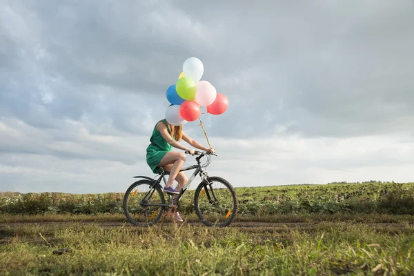 Chica joven montar en bicicleta con globos — Foto de Stock