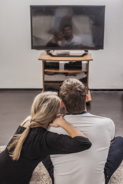 back view of adult caucasian couple sitting in their apartment and watching modern tv clipart