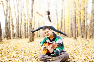 Arka planda sarı sonbahar orman genç kadın atlama sırasında akustik gitar çalmak genç İspanyol adam portresi