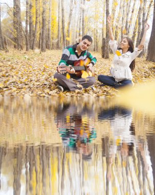 Kız ve erkek arka planda sarı sonbahar orman uçan ile akustik gitar çalmak portre bırakır.