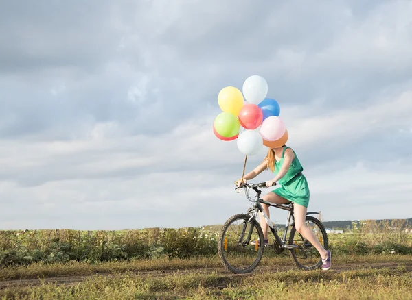 Mujer montando bicicleta y sosteniendo globos — Foto de Stock