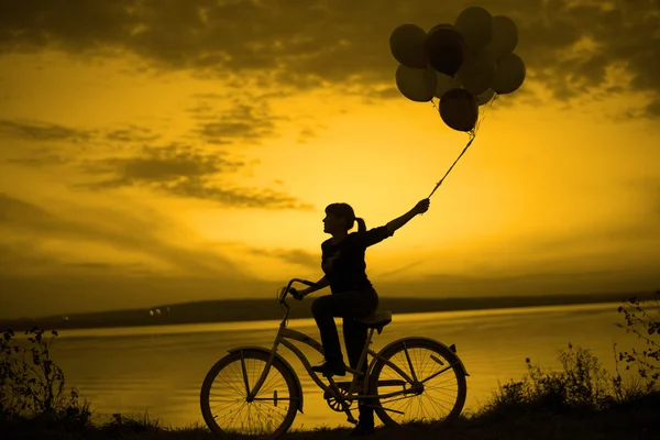 Chica en bicicleta celebración de globos de aire — Foto de Stock