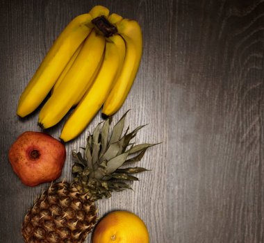  Bir ananas, greyfurt, nar ve taze muz. Üst Manzara. Siyah ahşap masa arka planı. Boş kopya alanı. sıra sağlıklı yiyecekler