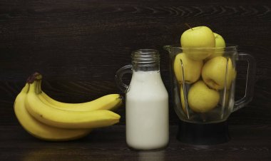 Ayakta duran süt şişesi ve taze muzların yanında sarı elmalarla dolu bir blender. Smoothie için malzemeler