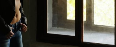  Siyah deri ceket ve kot pantolon giyen bir kadın. Pencerenin yanında duran kadın. Gün ışığı. Yüzü yok.