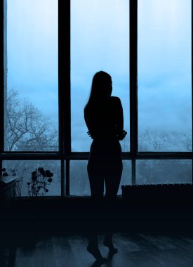 Pencerenin yanında duran kız silueti. Güzel bir kadın portresi. Ev rahatlığı. Duygular ve rahatlama. 