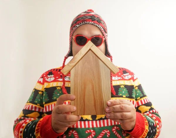 ニットセーターを着て小さな木造の家を保持している男 白地に隔離されてる お正月とメリークリスマス — ストック写真