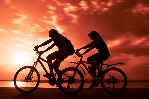 Sporty friends ride on bicycles. sunset sky. Silhouette of cyclist  on coast background. couple of people. 