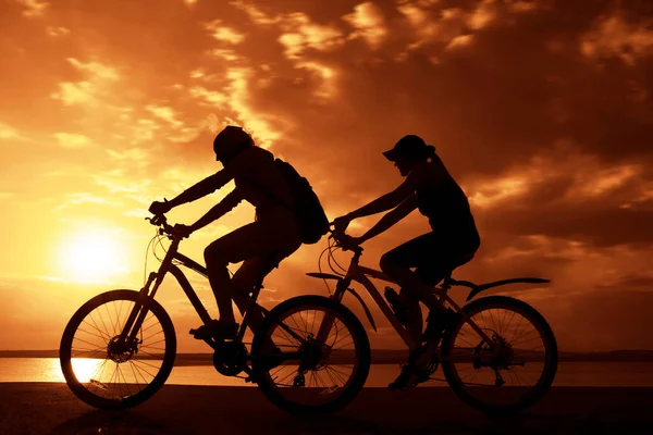 小气鬼朋友们骑自行车 日落的天空 海岸背景下骑自行车者的轮廓 两个人 — 图库照片